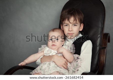 Portrait of older brother and younger sister, family, photo studio on gray background, children sit in chair
