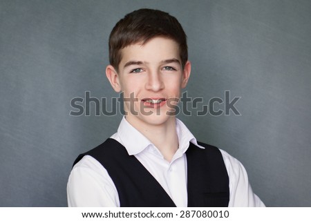Portrait of happy schoolboy teenager in white shirt and jacket against gray background