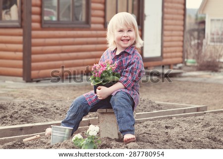 Little girl planting and watering flowers in garden on background of wooden house