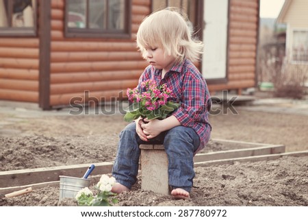 Little girl planting and watering flowers in garden on background of wooden house