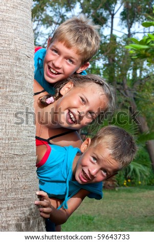 Three children look out from behind a palm, summer.