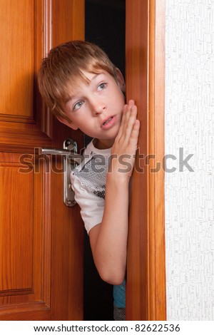 Surprised boy peeks from behind  door? indoor