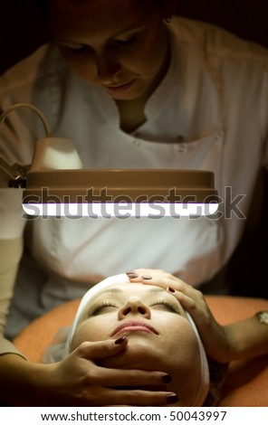 Woman in Cosmetic Cabinet under lamp. Faces skin cleaning. Dark tone.