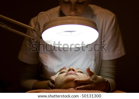 Woman in Cosmetic Cabinet under lamp. Faces skin cleaning. Dark tone.