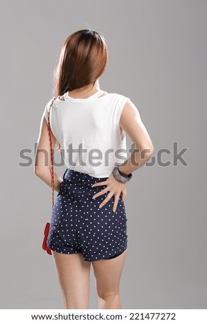 Asian woman posing in a white vest top and polka-dot shorts with red sling bag and bracelet in studio.