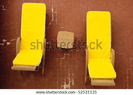 Overhead of a rattan table and two rattan deck chairs with yellow cushions. The table and chairs are on a brick patio.  Horizontal shot.