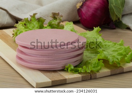 Cooked ham sausage with salad leaves on the wood background