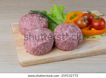 Raw burger cutlet with salad leaves on the wooden background