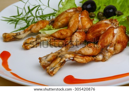 Fried frog legs with herbs on the wood background