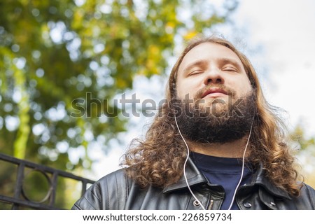 Blond long hair and beard young adult hipster man listening music. Outdoor, urban scene.