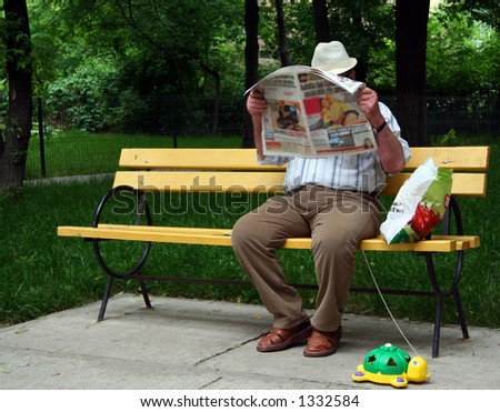 Man reads newspaper. Man in park on yellow bench with turtle.