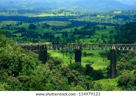 A stunning Indian landscape with a small railway bridge surrounded by greenery and mountains.