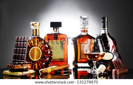 alcohol bottles and glass decorated chocolates and cigar on bar on gradient background