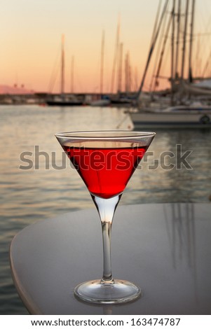 glass with the red cocktail on a background sea and boats