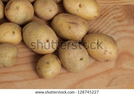 Fresh raw potatoes with potato peeler on wooden cutting board.