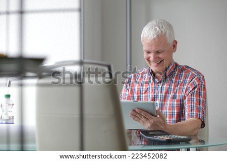Happy middle-aged Caucasian man using a high tech tablet PC connected to the internet, sitting at his desk