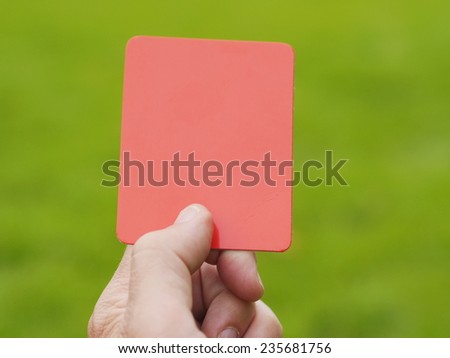 Hand holding up red card against soccer field