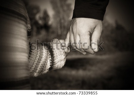 A parent holding the hand of its child while walking in a park............