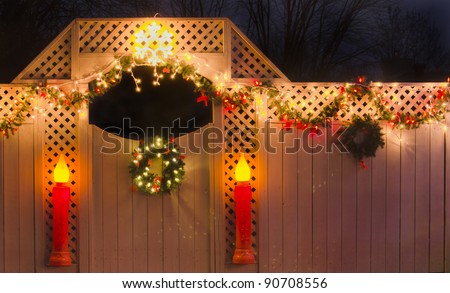 Christmas fence with garland, lights, wreaths and candles.