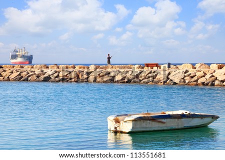 Old moored boat in the Red sea gulf fisherman fishing from a breakwater on the background of anchored huge cargo ship far on the horizon