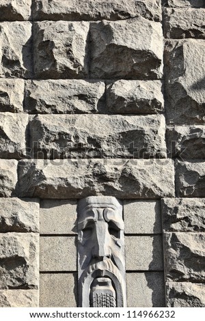 Granite stones wall decorated with bas relief of the old man\'s face. Residential building architecture of the early Soviet period, thirtieth year of the twentieth century