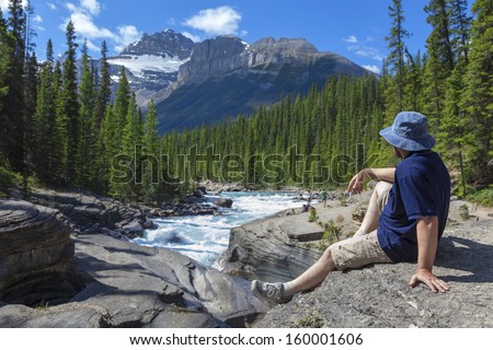 Tourist sitting on the brink of a canyon and looking at far mountains (Jasper National Park. Alberta. Canada)