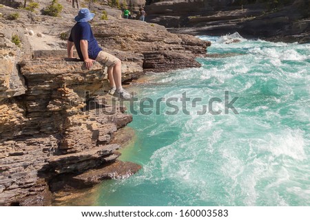 Tourist sitting on the brink of a canyon with the swift-flowing mountain river (Jasper National Park. Alberta. Canada)
