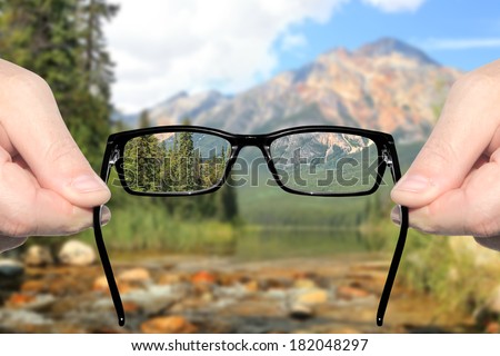 Hands holding and offering eye glasses to look at amazing mountain lake landscape.Sharp as a good sight symbol and unsharp as a bad sight symbol