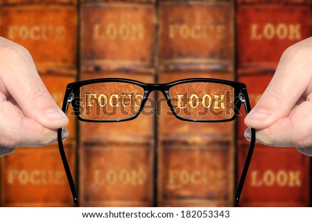 Sight test - optometrist's hands holding and offering eye glasses for the sharp look (in focus) on the books against the indistinct ( unsharp, not in focus) background. Concept of visual acuity return