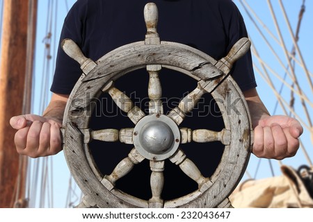 Old steering wheel in sailor hands with sailing tackles in the background