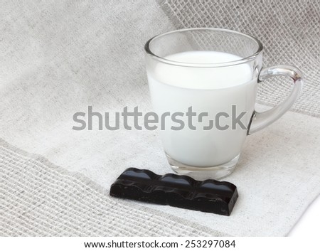 Glass mug of milk with dark chocolate chunk on linen cloth background