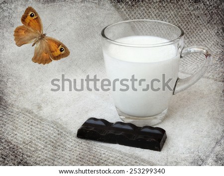 Glass mug of milk with dark chocolate chunk on linen cloth background and butterfly. Image done on old paper texture in decorative retro style