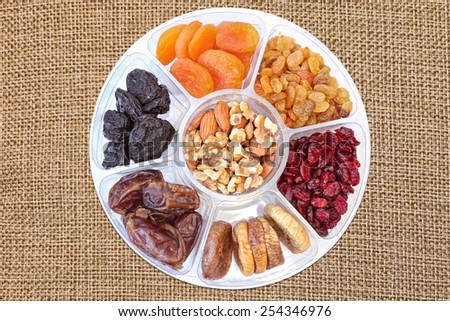 Dried fruits and nuts in plastic container for food storage. Raisin, cranberry, fig, plum, date, apricot fruits, walnuts and  almonds isolated on the canvas texture background