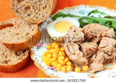 Canned tuna, sweet corn, boiled egg, sliced rye bread with bran and fresh salad leaves (rucola) on a bright color napkin