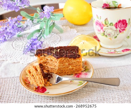 Honey cake with cream and chocolate glaze and elements of a tea drinking ceremony in the blurred background. Selective focus
