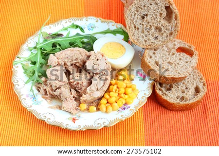 Canned tuna, sweet corn, boiled egg, sliced rye bread with bran and fresh salad leaves (rucola) on a bright color napkin.