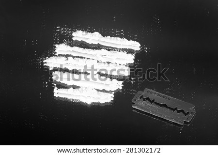 Cocaine powder in lines and razor blade on a grunge black background