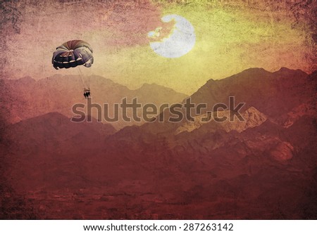 Parachute with people flying over the mountains. Paper texture. Aged textured photo in retro style