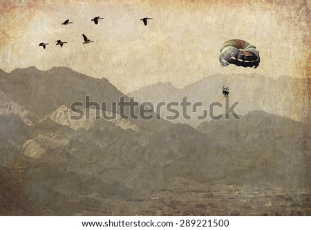 Parachute with people and migrating birds flying over the mountains. Paper texture. Aged textured photo in retro style