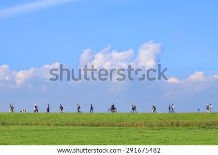 NETHERLANDS,MARKEN,OCTOBER 12,2014 : People walking on the road through a  dutch green meadow to the sea.This road is favorite for daily hiking for Marken\'s citizens and tourists (Marken,Netherlands)