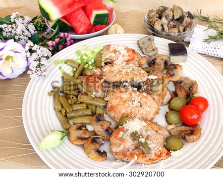 Grilled turkey fillet with grated cheese,green beans(snap beans),mushrooms and eggplants.Pickles and cherry tomato for garnish.Served with flowers and fruit.Mediterranean healthy food. Selective focus