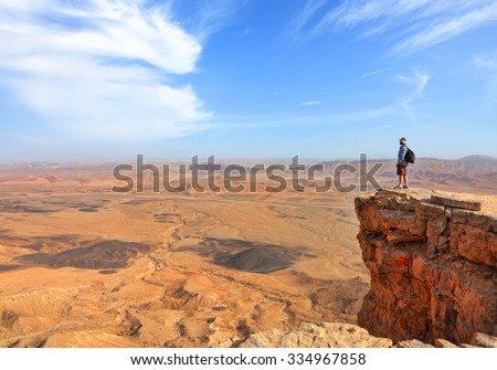 Panoramic view of color stone desert of Negev and traveler on the mountain top. National geological park HaMakhtesh HaGadol - Large Crater - a geological erosion land form, Israel
