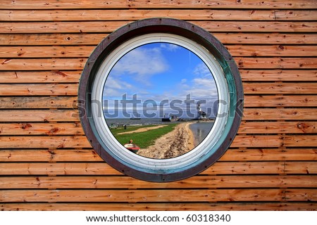 Round window of the wooden house with reflection of typical Holland landscape with a small lighthouse on seacoast (Marken. Netherlands)