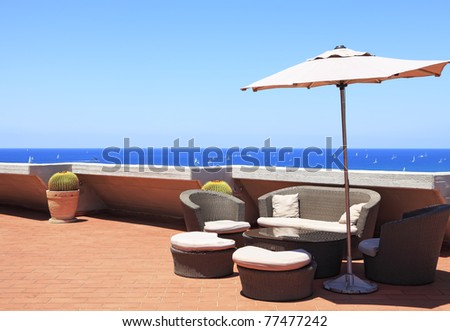 Corner of rest consisting of a sofa, summer armchairs and the padded stools located under an umbrella on an open veranda of a penthouse of hotel with a view on the Mediterranean sea