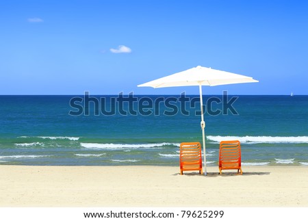 Two yellow chairs under a white umbrella on a sandy beach of Mediterranean sea