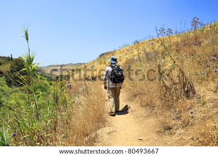 Tourist going to drought summer on edge of a ravine at which bottom streams not drying up stream and all green vegetation concentrates along this stream (Golan Heights. Israel)