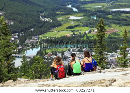 Three girls-tourists sitting on a grief and looking at a panorama of a small town Banff in a Bow river valley (Banff National Park. Alberta. Canada)