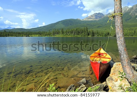 Old red canoe adhered to a tree on fine lake in an environment of mountains (Jasper National Park, Alberta, Canada)