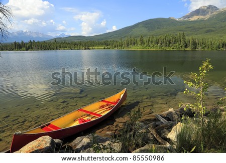 Old red canoe adhered to a tree on fine lake in an environment of mountains (Jasper National Park, Alberta, Canada)