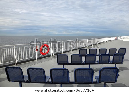 Dark blue chairs standing on a walking deck of the ferry, going through an ocean gulf on the cloudy sky and mountains background